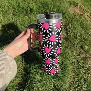 Detail of 40oz insulated tumbler with pink heart pattern and ergonomic handle on grass