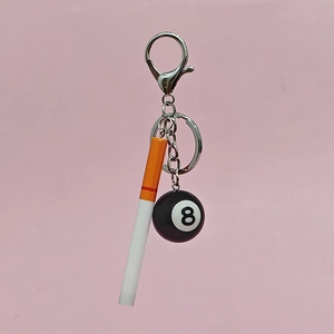 Miniature cigarette and black 8 pool ball keychain with metal lobster clasp on pink background