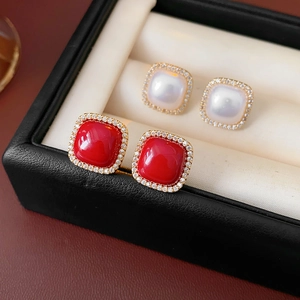 Close-up of gold-plated square stud earrings featuring pearl and red zircon centers