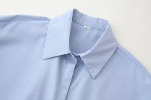 Detail view of the light blue shirt collar with ruffles and S size label on white background
