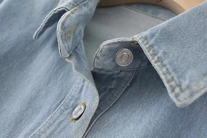 Detail of light blue denim shirt collar featuring metallic buttons and double stitching