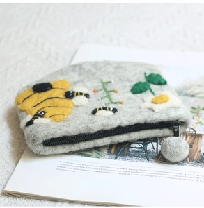 Detail of handmade wool felt bee coin purse with floral embroidery and fluffy pom pom zipper