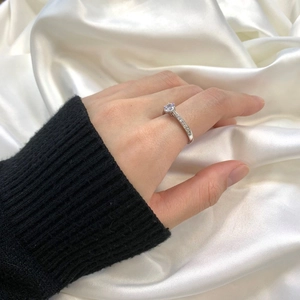 Close-up of classic 6-prong silver ring with a round diamond-cut stone on white satin