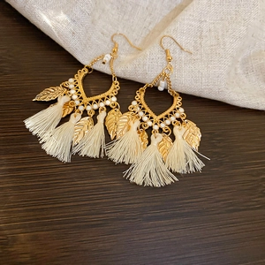 Detail of bohemian gold leaf earrings with white tassels and intricate bead accents