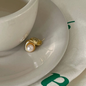 Close-up of golden irregular stud earrings with white freshwater pearl on ceramic dish