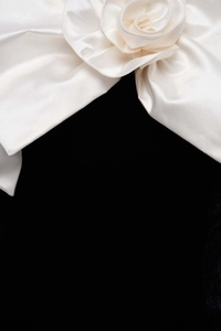 Detail of a large white satin bow with a 3D handmade rose flower on black fabric