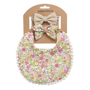 Detail of floral baby bib with white pom-pom trim and two matching bow headbands