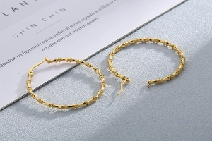 Detail view of large gold bamboo textured hoop earrings on a minimalist grey surface