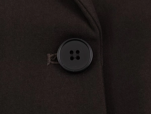 Detail of the black four-hole button and twill fabric texture on a brown blazer set
