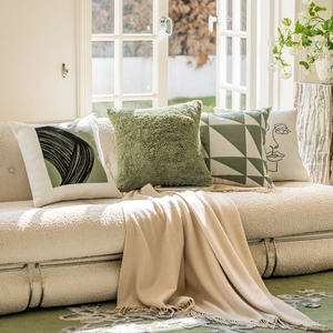 Close-up of beige and green luxury pillows and a knit blanket on a teddy fleece sofa