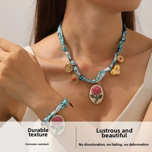Detail of blue fabric tie-dye necklace with pink rose cameo and gold heart charms