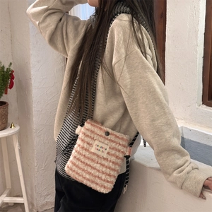 Close-up of plush striped crossbody bag with fabric label and woven strap detail