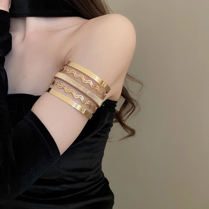Detailed view of layered gold metal arm cuffs with wavy and textured minimalist design