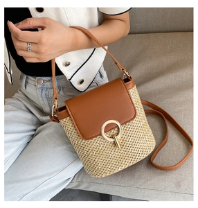 Close-up of a woven straw bucket bag with brown leather flap and round metal lock
