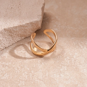Detail of adjustable gold-colored X-shaped ring with textured rock background