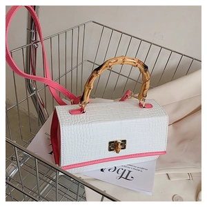Detail of white crocodile texture handbag with pink trim and bamboo handle in a shopping cart