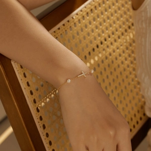 Close-up of golden cross bracelet with white pearls and diamonds on a female wrist
