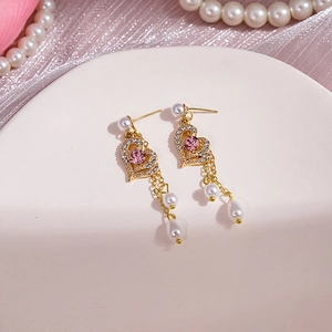 Détail de boucles d'oreilles cœur dorées avec cristaux roses et perles sur soie
