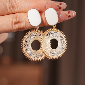 Close-up of gold lattice circle earrings with white enamel detail held by hand