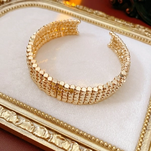 Gros plan d'un bracelet manchette doré à quatre rangées de perles sur velours blanc