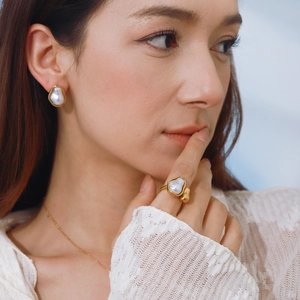 Detail of model wearing gold-plated irregular pearl earrings and ring set in soft light