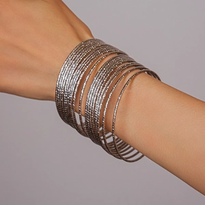 Dettaglio del set di 20 bracciali metallici a strati con texture opaca su modella