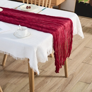 Elegant deep red wrinkled cheesecloth table runner with white tasseled waffle fabric