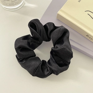 Close-up of premium black satin scrunchie with silky texture and elegant pleats