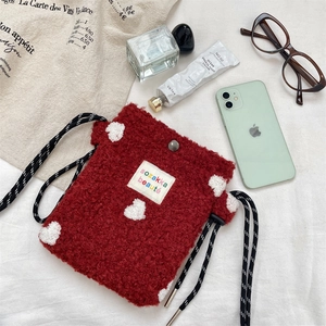 Flat lay of red plush crossbody bag with white heart embroidery and woven strap