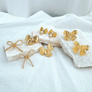 Detailed view of various gold bow earrings with pearls and crystals on white display