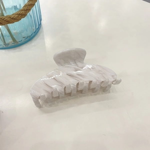 Macro shot of large acetate hair claw clip with white marble pattern on white surface