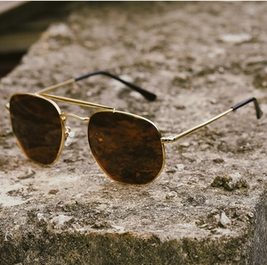 Detail of polarized aviator sunglasses with gold metal frame on a rugged rock background