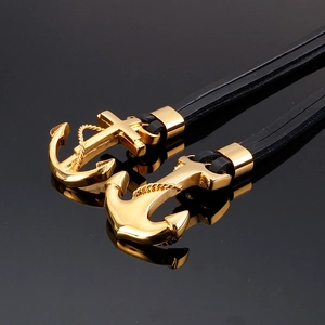 Macro shot of gold anchor and cross charms on black multi-layer braided leather bracelets