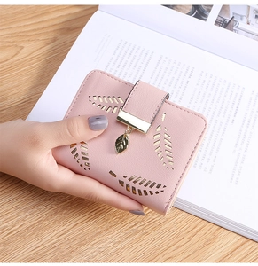Pink short wallet with hollow leaf design and gold pendant detail on a wooden table