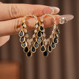 Detailed view of heart-shaped gold earrings with black teardrop gemstones on ear