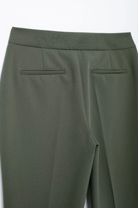 Macro d'un pantalon vert foncé montrant les poches passepoilées et le tissu sergé