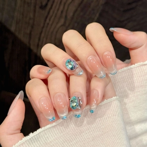 Close-up of pink gradient press-on nails with luxury blue rhinestones on model's hand