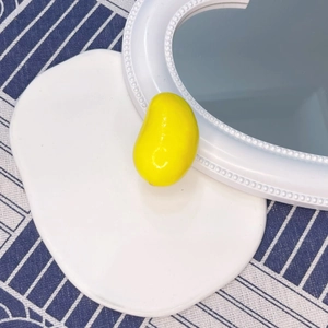 Detail shot of a glossy yellow mango food hair clip on a white tray with blue striped cloth