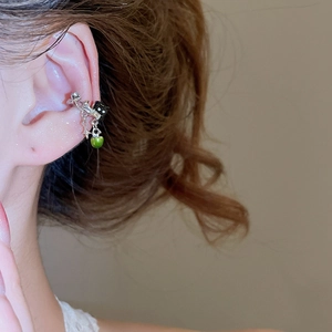 Close-up of silver star ear cuff with black cat and green bead charm on ear