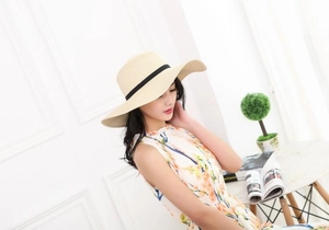 Detail of beige wide-brim straw sun hat with black ribbon worn by a model in bright setting