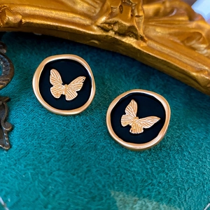 Close-up of vintage butterfly stud earrings in matte black and gold finish on green velvet