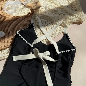 Detail of cross-back straps and scalloped embroidery on a one-piece black swimsuit