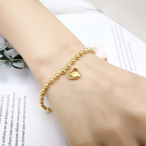 Detailed close-up of a gold beaded bracelet featuring a minimalist heart pendant on a wrist