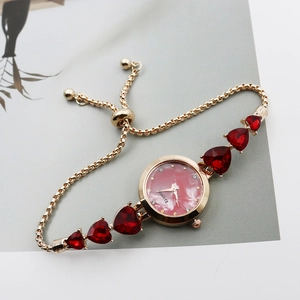 Detail of gold women's watch with red heart gemstones and pink marble dial texture