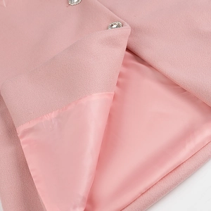 Gros plan d'un manteau en laine rose montrant un bouton diamant et une doublure soyeuse