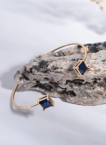 Detail of gold open bracelet featuring blue square zircon set on a textured stone base