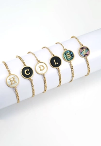 Detailed view of gold stainless steel bracelets with assorted shell letter charms on props