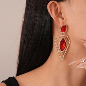 Close-up of geometric gold drop earrings with diamond-encrusted red rhombic crystals
