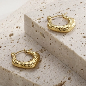 Detail of golden C-shaped earrings with irregular hammered texture on beige porous stones