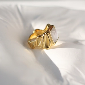 Macro detail of 18K gold-plated ring with liquid wave texture and square white shell stone